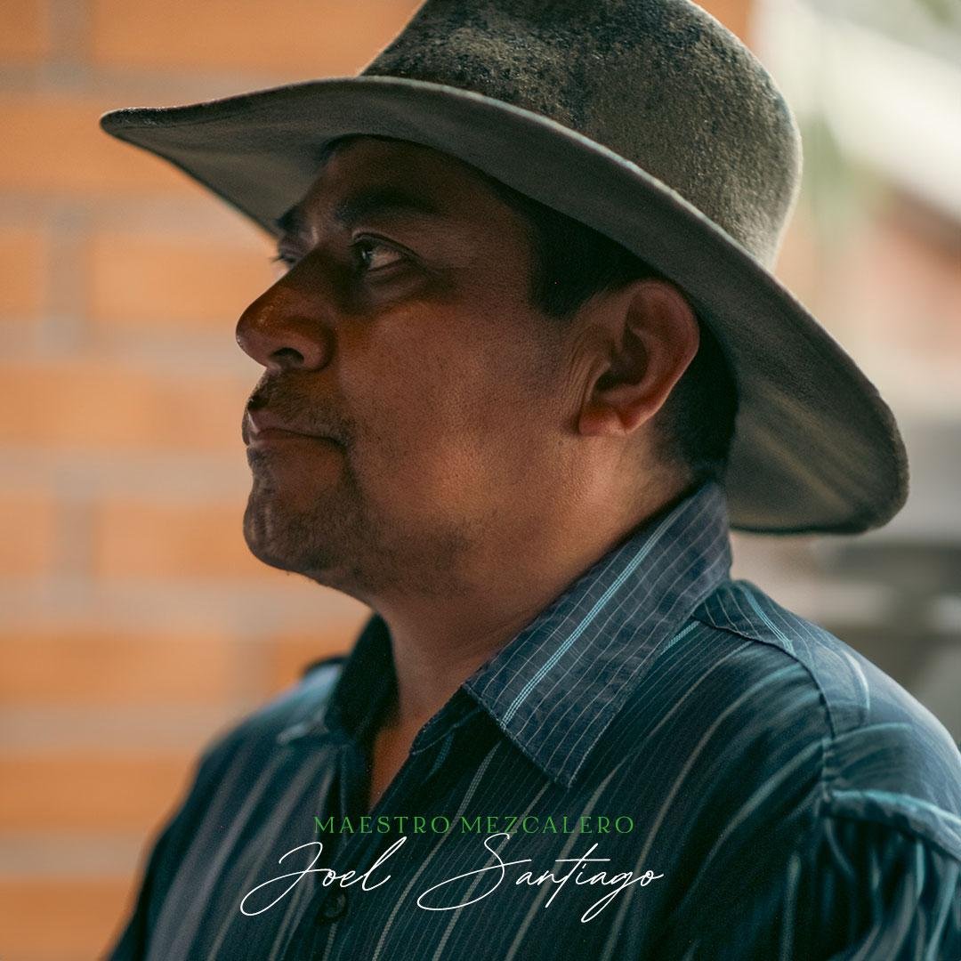 Joel Santiago, maestro mezcalero, de perfil con sombrero, ante un muro de ladrillo